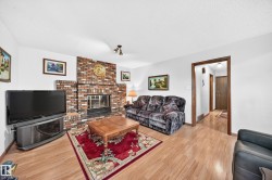 Living area featuring a brick fireplace with a raised hearth, wood-finish flooring, white walls, and dark wood trim - 