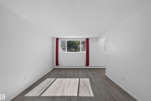 Bright interior featuring wood-finish flooring, white walls, and a large window - 6 10230 122 Street Nw, Edmonton, AB 
