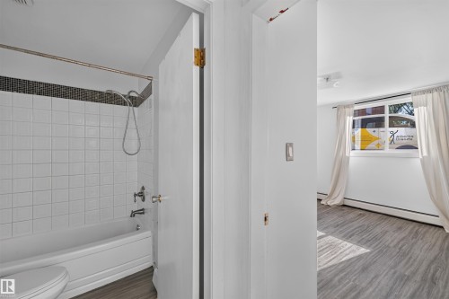 Bathroom featuring white subway tile surround with a dark mosaic accent, white bathtub, and chrome fixtures - 6 10230 122 Street Nw, Edmonton, AB 