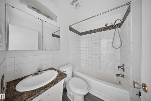 Bathroom featuring a white subway tile tub surround with a mosaic tile accent, a vanity with a dark speckled countertop, and an integrated white sink - 6 10230 122 Street Nw, Edmonton, AB 