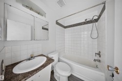 Bathroom featuring a white subway tile tub surround with a mosaic tile accent, a vanity with a dark speckled countertop, and an integrated white sink - 