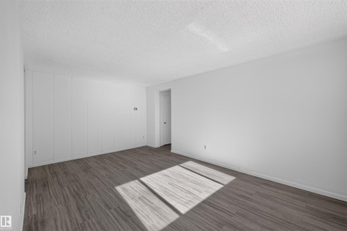 Spacious room featuring wood-finish flooring, white walls, and a textured white ceiling - 6 10230 122 Street Nw, Edmonton, AB 