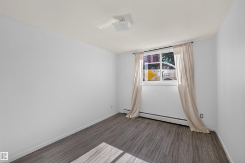 Room featuring wood-finish flooring, a white ceiling, and white painted walls - 6 10230 122 Street Nw, Edmonton, AB 