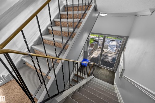 Stairwell featuring metal railings with a brass-finish top rail, light gray painted walls, and textured stair treads - 6 10230 122 Street Nw, Edmonton, AB 