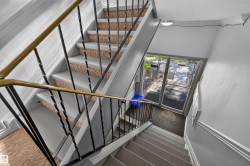 Stairwell featuring metal railings with a brass-finish top rail, light gray painted walls, and textured stair treads - 