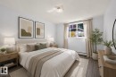Bedroom featuring wood-finish flooring, a window with natural light, neutral wall paint, a ceiling-mounted light fixture, and baseboard heating - 6 10230 122 Street Nw, Edmonton, AB 