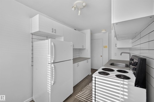 Compact kitchen featuring white cabinetry, a stainless steel sink, a full-size refrigerator, an electric range, and wood-finish flooring - 6 10230 122 Street Nw, Edmonton, AB 
