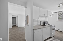 Compact kitchen featuring white cabinetry with brushed nickel hardware, a stone-finish countertop, stainless steel sink with a gooseneck faucet, and a subway tile backsplash - 