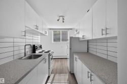 Galley kitchen featuring white cabinetry, gray speckled countertops, a stainless steel sink with a matte black faucet, and a white subway tile backsplash - 