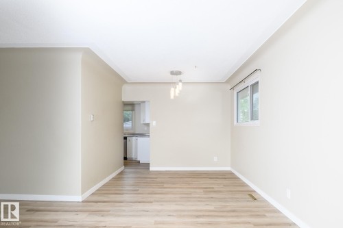 Open-concept living area featuring wood-finish flooring, a modern multi-bulb light fixture, a window with natural light, neutral wall colors, and white baseboards - 9607 75 Street, Edmonton, AB 