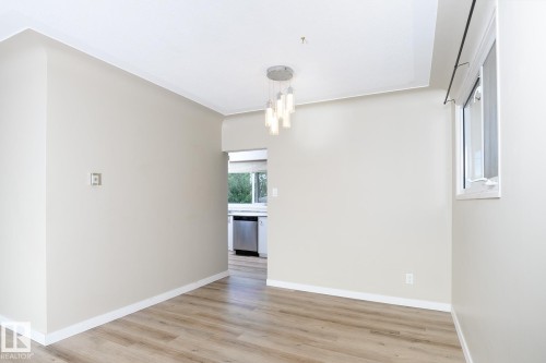 Open concept living area featuring wood-finish flooring, neutral wall tones, and a modern multi-light pendant fixture - 9607 75 Street, Edmonton, AB 
