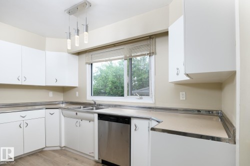 Kitchen featuring white cabinetry with silver-tone hardware, wood-finish flooring, and a stainless steel dishwasher - 9607 75 Street, Edmonton, AB 