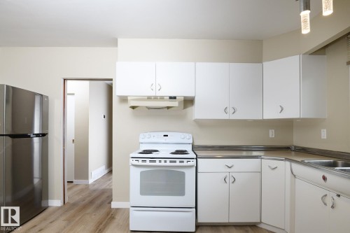 Kitchen featuring white cabinetry with silver hardware, white range, stainless steel refrigerator, and wood-finish flooring - 9607 75 Street, Edmonton, AB 