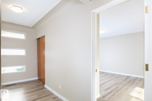 Entryway featuring light wood-finish flooring, three horizontal translucent windows, a built-in wood-finish sliding door, and a flush-mount ceiling light fixture - 9607 75 Street, Edmonton, AB 