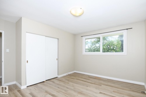 Interior room featuring a large horizontal window, wood-finish flooring, white baseboards, and a built-in closet with sliding doors - 9607 75 Street, Edmonton, AB 