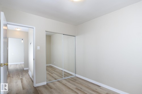 Room featuring light wood-finish flooring, neutral wall paint, white trim, and a full-length mirrored closet with sliding doors - 9607 75 Street, Edmonton, AB 