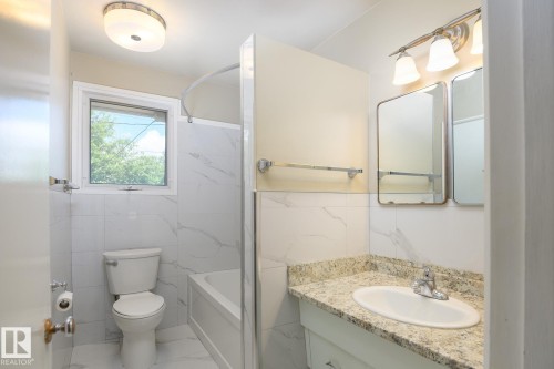Bathroom featuring white subway tile surround, integrated shower/tub combination, granite-finish countertop, and a vanity with built-in storage - 9607 75 Street, Edmonton, AB 