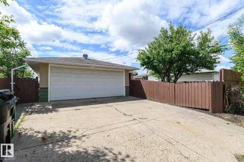 Detached garage with a white panel door, concrete driveway, and brown wood privacy fencing - 9607 75 Street, Edmonton, AB 