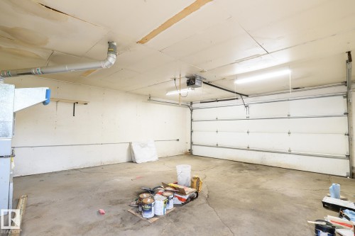 Spacious garage featuring a sectional overhead door, concrete flooring, and ceiling-mounted fluorescent lighting - 9607 75 Street, Edmonton, AB 
