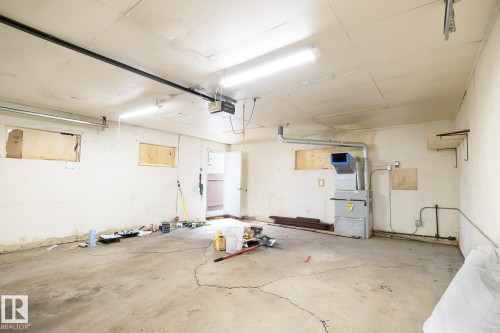 Spacious garage featuring a concrete floor, built-in shelving brackets, fluorescent lighting, and visible HVAC system - 9607 75 Street, Edmonton, AB 