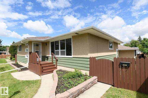 Exterior featuring a combined stucco and horizontal siding facade, a front wooden deck with steps and railings, and a privacy fence with a gate - 9607 75 Street, Edmonton, AB 