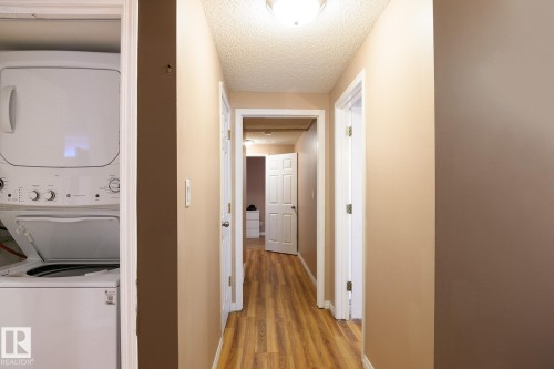 Dedicated laundry closet featuring a stacked washer and dryer, wood-finish flooring, and neutral wall tones - 9607 75 Street, Edmonton, AB 