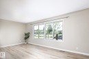 Bright interior space featuring a large multiple-pane window, light wood-finish flooring, white baseboards, and neutral wall paint - 9607 75 Street, Edmonton, AB 