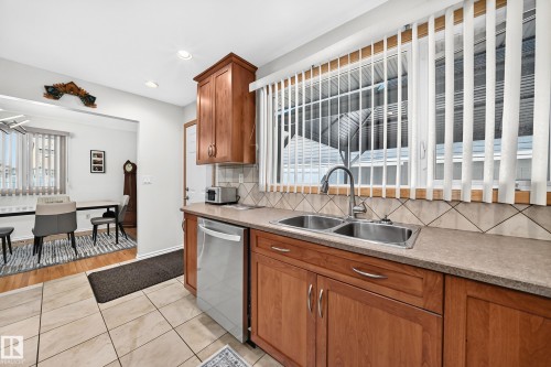 Kitchen featuring wood cabinetry, stainless steel double basin sink, and a tile backsplash - 11708 138 Avenue Nw, Edmonton, AB 