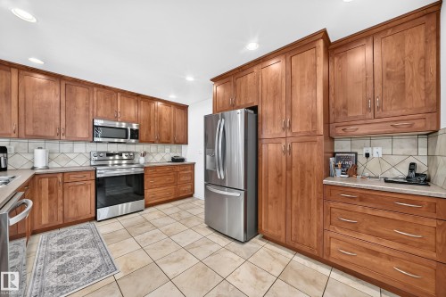 Kitchen featuring extensive wood cabinetry, stainless steel appliances, tiled backsplash, light-toned countertops, and tiled flooring - 11708 138 Avenue Nw, Edmonton, AB 