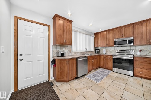 Kitchen featuring warm wood cabinetry, stainless steel appliances, tile flooring, and a patterned tile backsplash - 11708 138 Avenue Nw, Edmonton, AB 