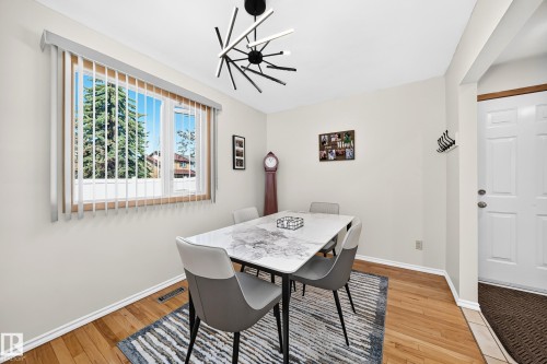 Dining area featuring hardwood flooring, a modern linear chandelier, and a large window with vertical blinds - 11708 138 Avenue Nw, Edmonton, AB 