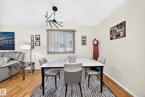 Bright dining area featuring wood-finish flooring, a contemporary chandelier, and a large window with vertical blinds - 11708 138 Avenue Nw, Edmonton, AB 