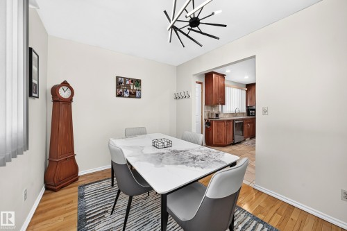 Dining area featuring wood-finish flooring, a modern linear chandelier, and light-toned walls - 11708 138 Avenue Nw, Edmonton, AB 