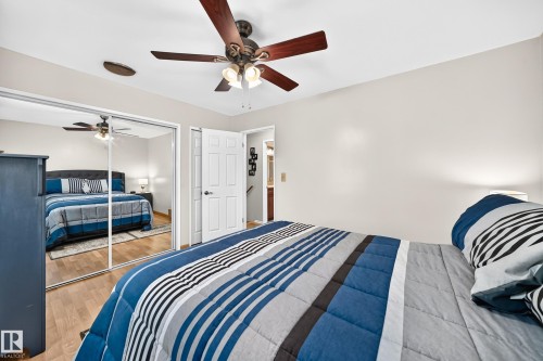 Bedroom featuring wood-finish flooring, mirrored sliding closet doors, and a ceiling fan with integrated lighting - 11708 138 Avenue Nw, Edmonton, AB 