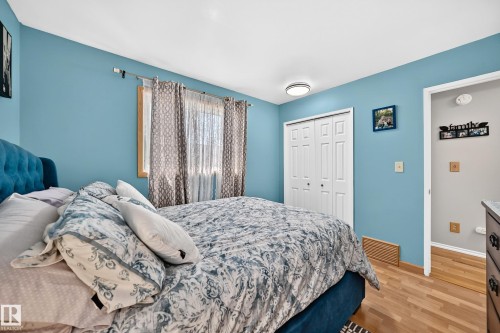 Bedroom featuring light blue walls, wood-finish flooring, a window with natural wood trim, and a bi-fold closet door - 11708 138 Avenue Nw, Edmonton, AB 