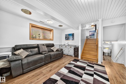 Open living space featuring wood-finish flooring, white paneled ceilings, and a light wood-framed window with blinds - 11708 138 Avenue Nw, Edmonton, AB 