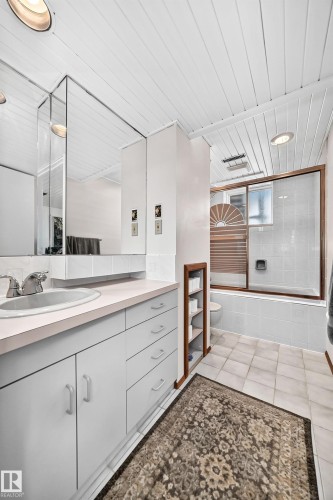 Vanity with integrated sink and chrome faucet, set against a mirrored wall and white subway tile backsplash - 11708 138 Avenue Nw, Edmonton, AB 