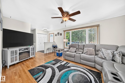 Living area featuring wood-finish flooring, a ceiling fan with integrated lighting, and a large window with vertical blinds - 11708 138 Avenue Nw, Edmonton, AB 