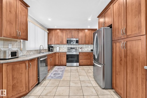 Kitchen featuring extensive wood cabinetry, stainless steel appliances, tile flooring, and a tile backsplash - 11708 138 Avenue Nw, Edmonton, AB 