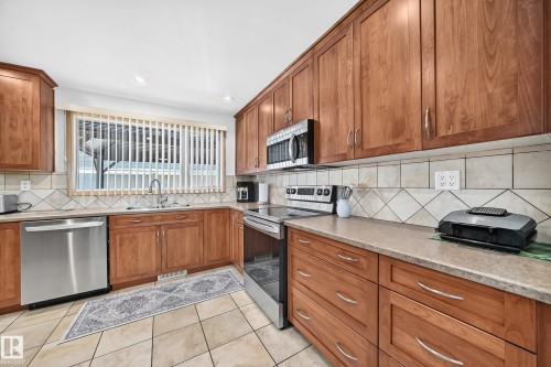 Kitchen featuring wood-finish cabinetry, stainless steel appliances, a tile backsplash with diamond accents, and a window above the sink - 11708 138 Avenue Nw, Edmonton, AB 