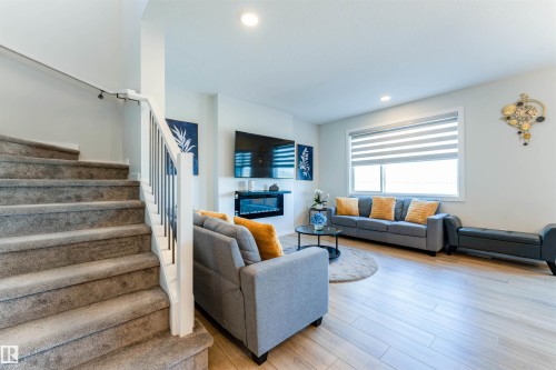 Carpeted staircase with white newel post and dark metal spindles - 8426 228A Street Nw, Edmonton, AB - Indoor Photo Showing Living Room With Fireplace