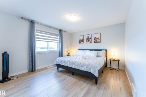 Bedroom featuring light wood-finish flooring, a large window with roller shades and drapery, and neutral wall tones - 8426 228A Street Nw, Edmonton, AB - Indoor Photo Showing Bedroom