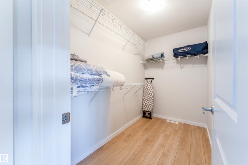 Walk-in closet featuring light wood-finish flooring, white wire shelving, and a bright overhead light fixture - 8426 228A Street Nw, Edmonton, AB - Indoor With Storage