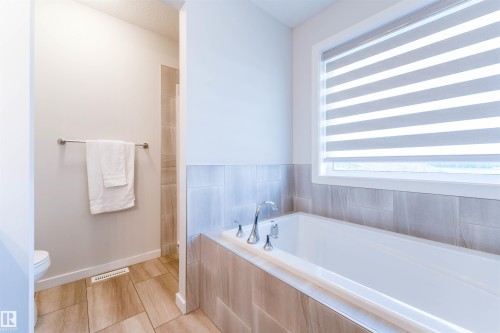 Soaking tub with deck-mounted chrome fixtures and light wood-finish tile surround - 8426 228A Street Nw, Edmonton, AB - Indoor Photo Showing Bathroom