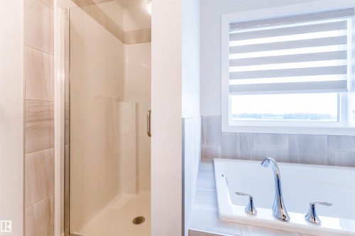 Freestanding soaking tub with chrome fixtures, a privacy window with banded shades, and a glass-enclosed standing shower with tiled walls - 8426 228A Street Nw, Edmonton, AB - Indoor Photo Showing Bathroom