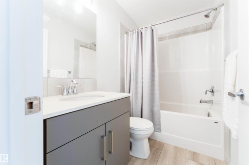 Bathroom featuring a white bathtub with shower, a gray vanity with a white countertop, a recessed sink, chrome fixtures, and wood-finish flooring - 8426 228A Street Nw, Edmonton, AB - Indoor Photo Showing Bathroom