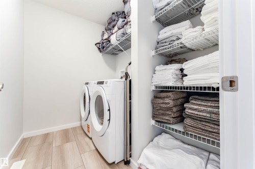 Dedicated laundry area featuring wood-finish flooring, white walls, and a stacked washer and dryer - 8426 228A Street Nw, Edmonton, AB - Indoor Photo Showing Laundry Room