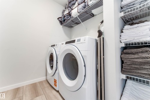 Dedicated laundry area featuring modern white appliances, wood-finish flooring, white walls, and built-in wire shelving for organized storage - 8426 228A Street Nw, Edmonton, AB - Indoor Photo Showing Laundry Room