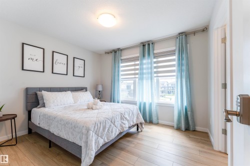 Bedroom featuring wood-finish flooring, a contemporary flush-mount ceiling light, and three windows with blinds and curtain rods - 8426 228A Street Nw, Edmonton, AB - Indoor Photo Showing Bedroom