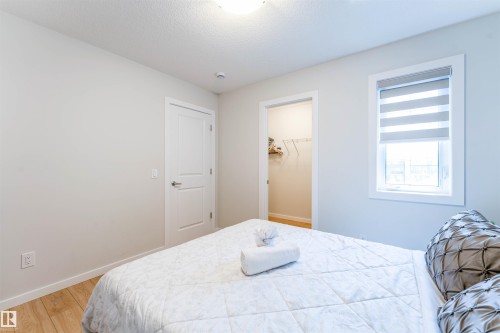 Bedroom featuring light wood-finish flooring, a white trim window with roller shade, and a walk-in closet with wire shelving - 8426 228A Street Nw, Edmonton, AB - Indoor Photo Showing Bedroom